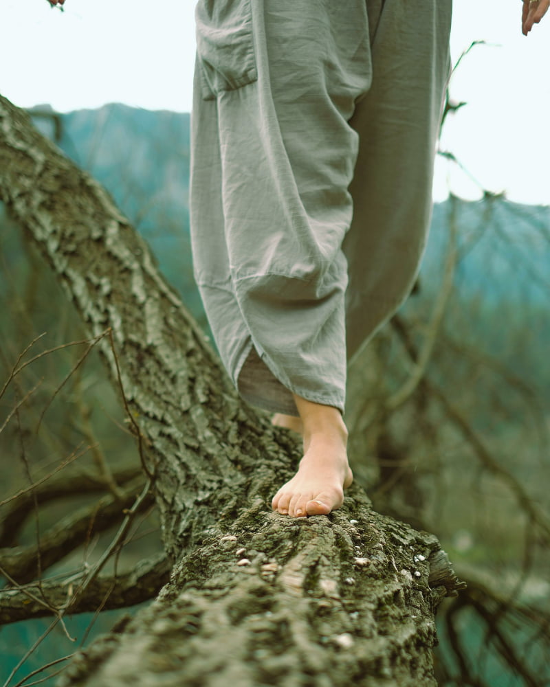 Barefoot woman balancing on a tree branch, showing sensory awareness and balance through the feet