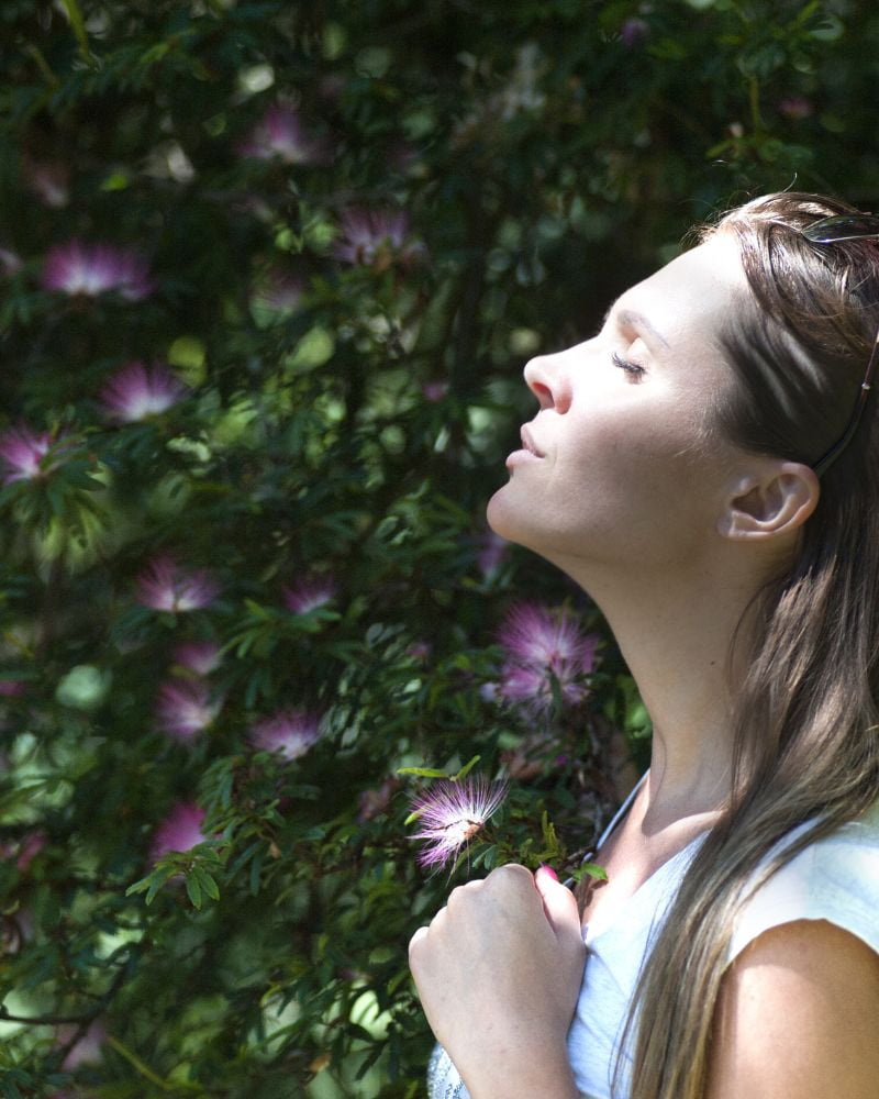 Woman standing outdoors with eyes closed, breathing calmly and reconnecting with the body